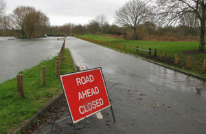 Photograph showing a warning sign in front of a flooded country road.
