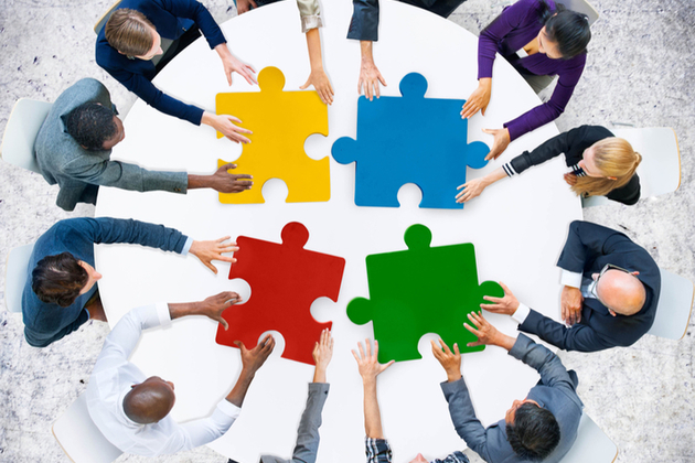 large jigsaw pieces being brought together by people on a round table