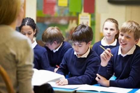 Children sitting in a classroom with a teacher present at the front.