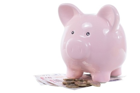 Pink piggy bank with coins and notes at its feet