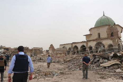 Men in flak jackets walk among the rubble of buildings in Mosul.