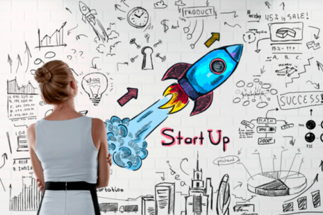 Women looking at a wall full of brainstorming graffiti including the word start-up