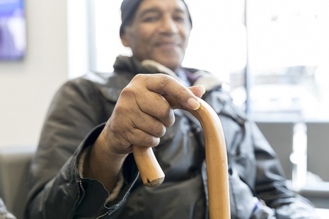 An elderly man with a walking stick, smiling.
