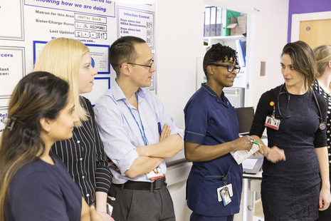 health professionals have stand up meeting in hospital corridor