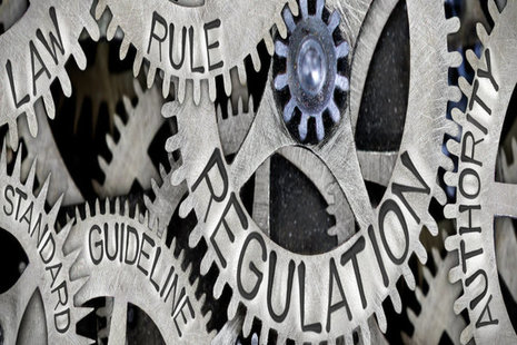 An image of interlinked metal cogs featuring words such as law, regulation.