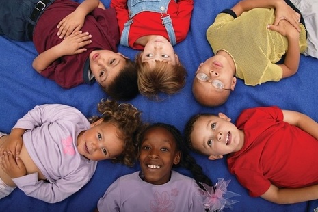 6 children lying in a circle, heads touching, on a blue background