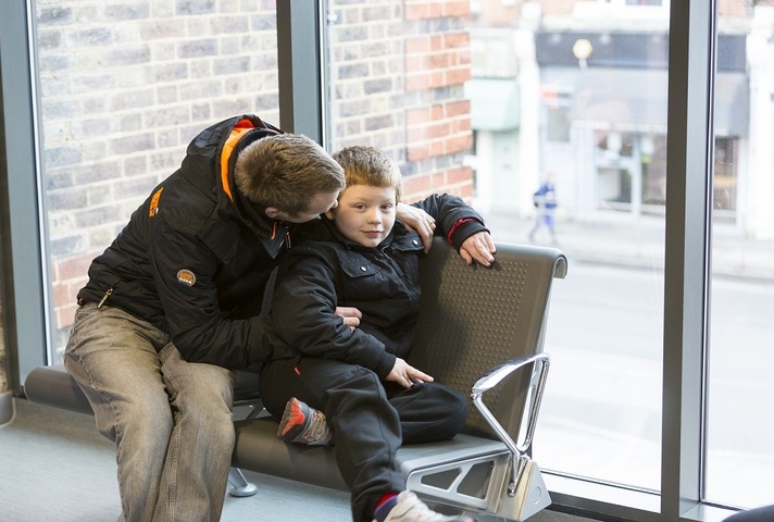 A father giving his young son a hug in a doctors' waiting area.