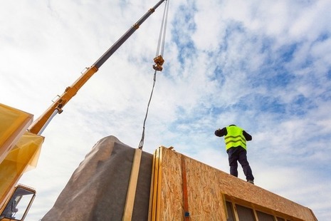 Construction worker guides a crane lifting a modular structure