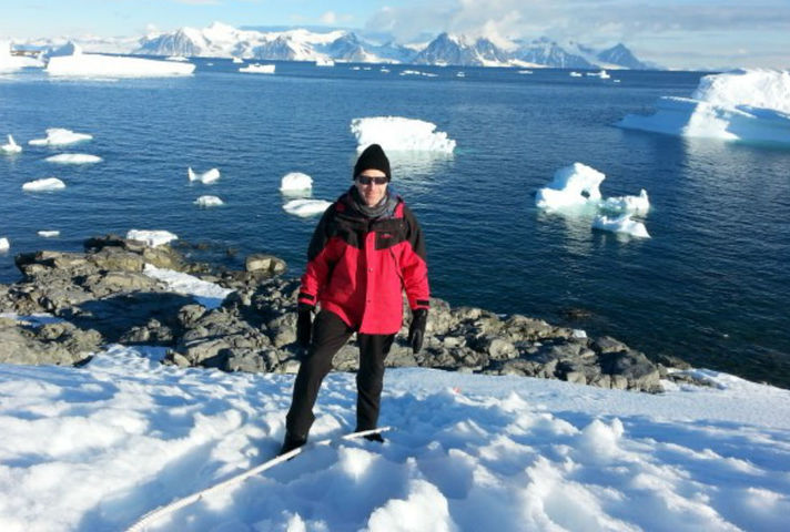 Ben Merrick pictured in Antarctica, dressed in cold-weather gear and with the sea and icebergs in the background.