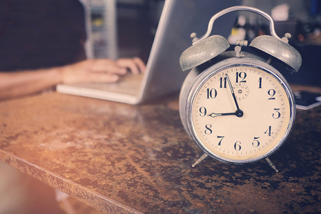 Clock with person typing on laptop in the background