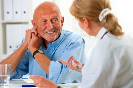 A doctor talks with a senior male patient via Alexander Raths at Shutterstock
