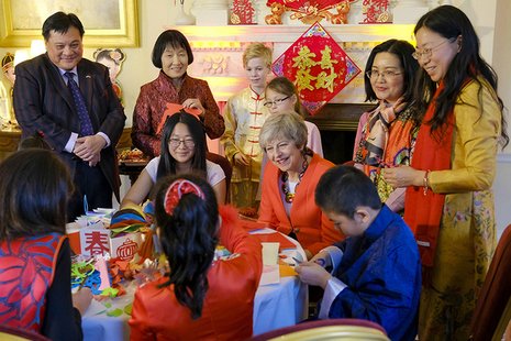 Prime Minister Theresa May sitting at table with children doing paper cutting exercise at Chinese New Year reception