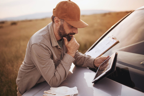 An image of a man reading a tablet in a field.