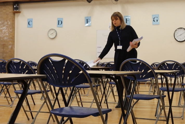 A woman handing out papers in an empty exam hall