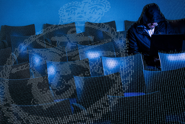A hacker sits in the shadows working on a laptop