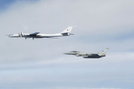 An RAF Typhoon flys alongside a Russian bomber jet in a blue and cloudy sky