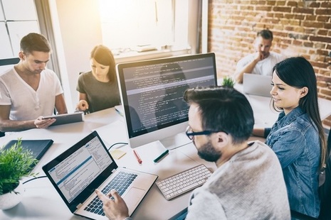 Group of men and women sitting round a desk working on computers