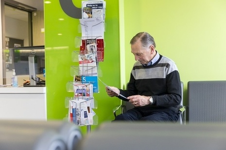 An older man sitting in a GP waiting area reading a leaflet