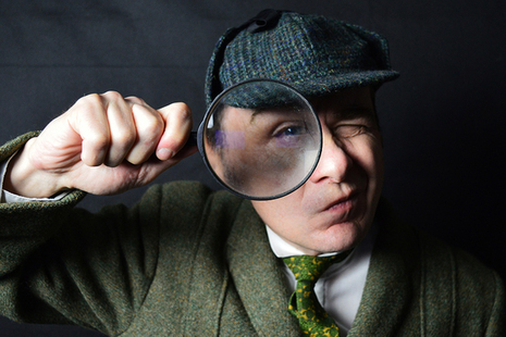 An actor dressed as Sherlock Holmes holding a magnifying glass