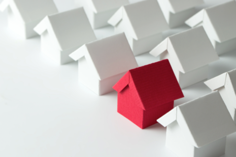 A red paper house placed alongside rows of white papers houses