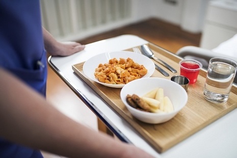 Close-up of a nurse carrying a tray of cereal, fruit, fruit juice and water