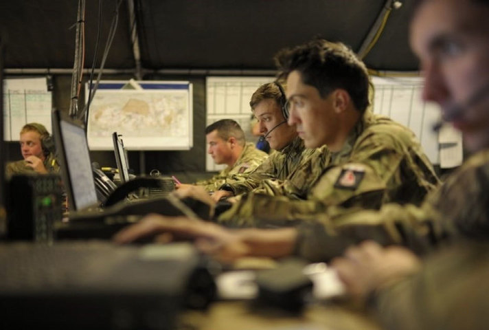 Battlegroup Headquarters with soldiers sitting at a desk some with headsets looking at computers.