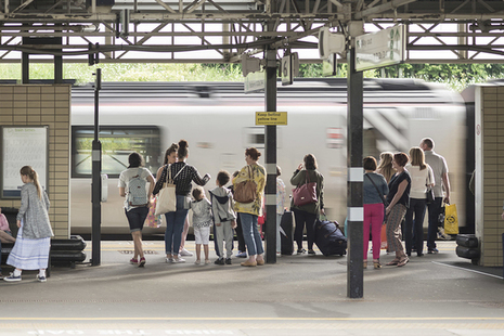 Group of rail passengers with luggage waiting on station platform as a train pulls in