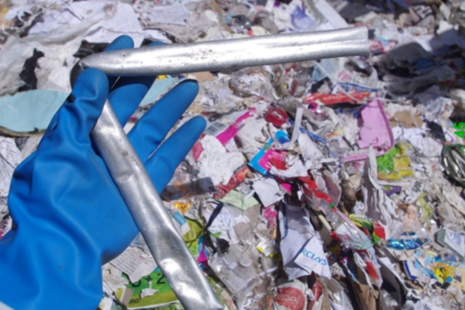 Hand in a blue glove holding a bent metal pipe with waste in the background