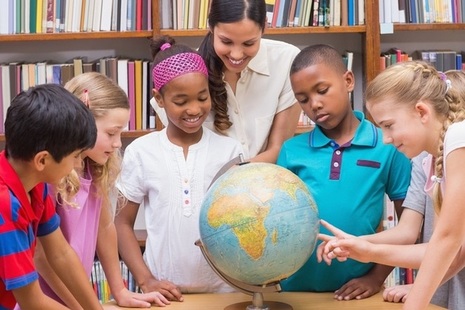 Group of children with their teacher in a library looking at a globe