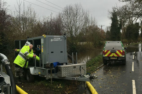 An Environment Agency officer operating a water pump beside a road with an EA vehicle in the background