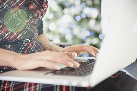 A woman with a laptop in front of a Christmas tree with blue lights.