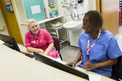 Two nurses talking and smiling at a reception desk