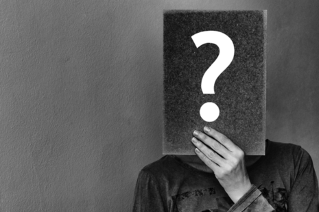 A person holding a card in front of their face with a question mark on it.