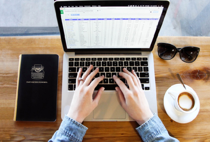 Hands typing on laptop keyboard with computer screen showing spreadsheet