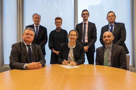 People sitting and standing around table signing a contract