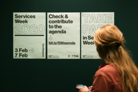 Woman looking at services week 2020 posters.