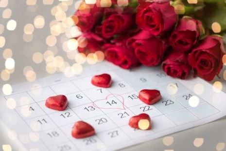 A calendar with 14 February circled in a love heart next to a bouquet of roses and heart shaped chocolates in red foil.