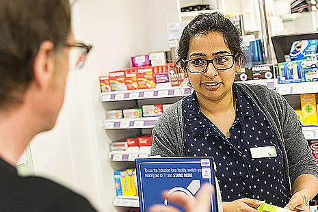 A pharmacist and a man talk over the counter in a pharmacy