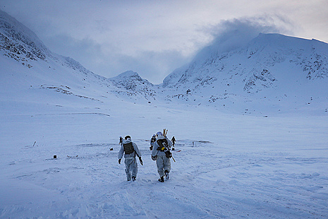 Royal Marines clad in white uniforms march against a backdrop of snowy hills and an ice blue sky