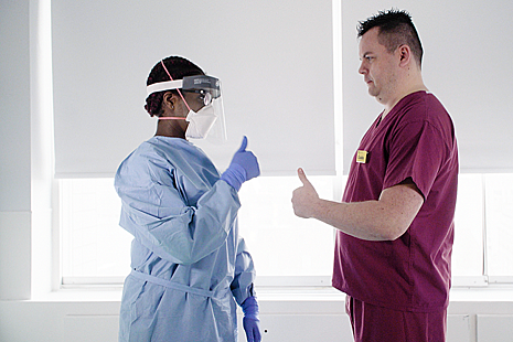 Two professionals in a clinical setting wearing PPE