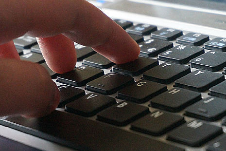 Stock image of a hand typing on a laptop.