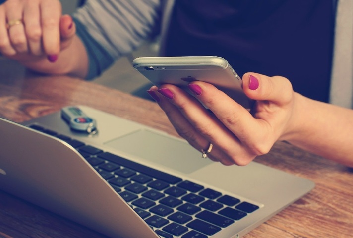 Woman sitting at laptop and looking at mobile phone
