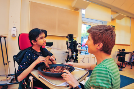 A carer conducting a sensory experience, with a bowl of leaves, for a girl with SEND