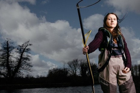 A female Environment Agency employee stands with an electro-fishing rod by a lake