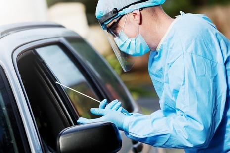 Tester in PPE holding swab next to car window