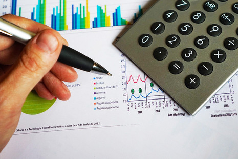 Hand with pen and graphs and charts in the background.