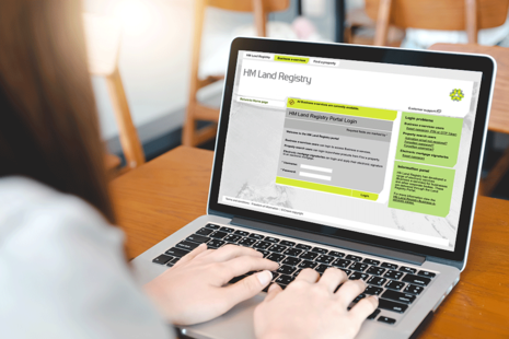 Laptop user types on keyboard with screen showing the HM Land Registry portal home page.