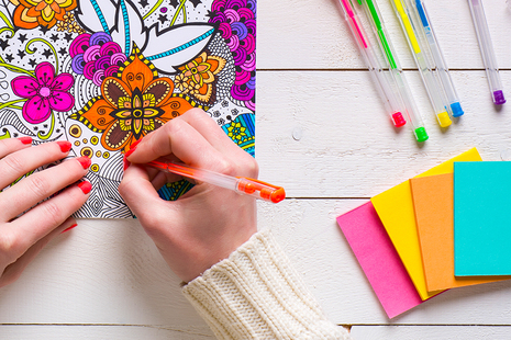 Hands of a person colouring in a mental wellbeing colouring book with a pen