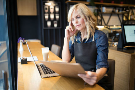 Woman sitting at a laptop consulting a document.