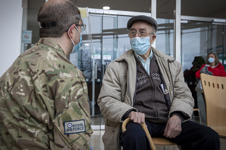 Image depicts a soldier sitting and speaking with an elderly gentleman.